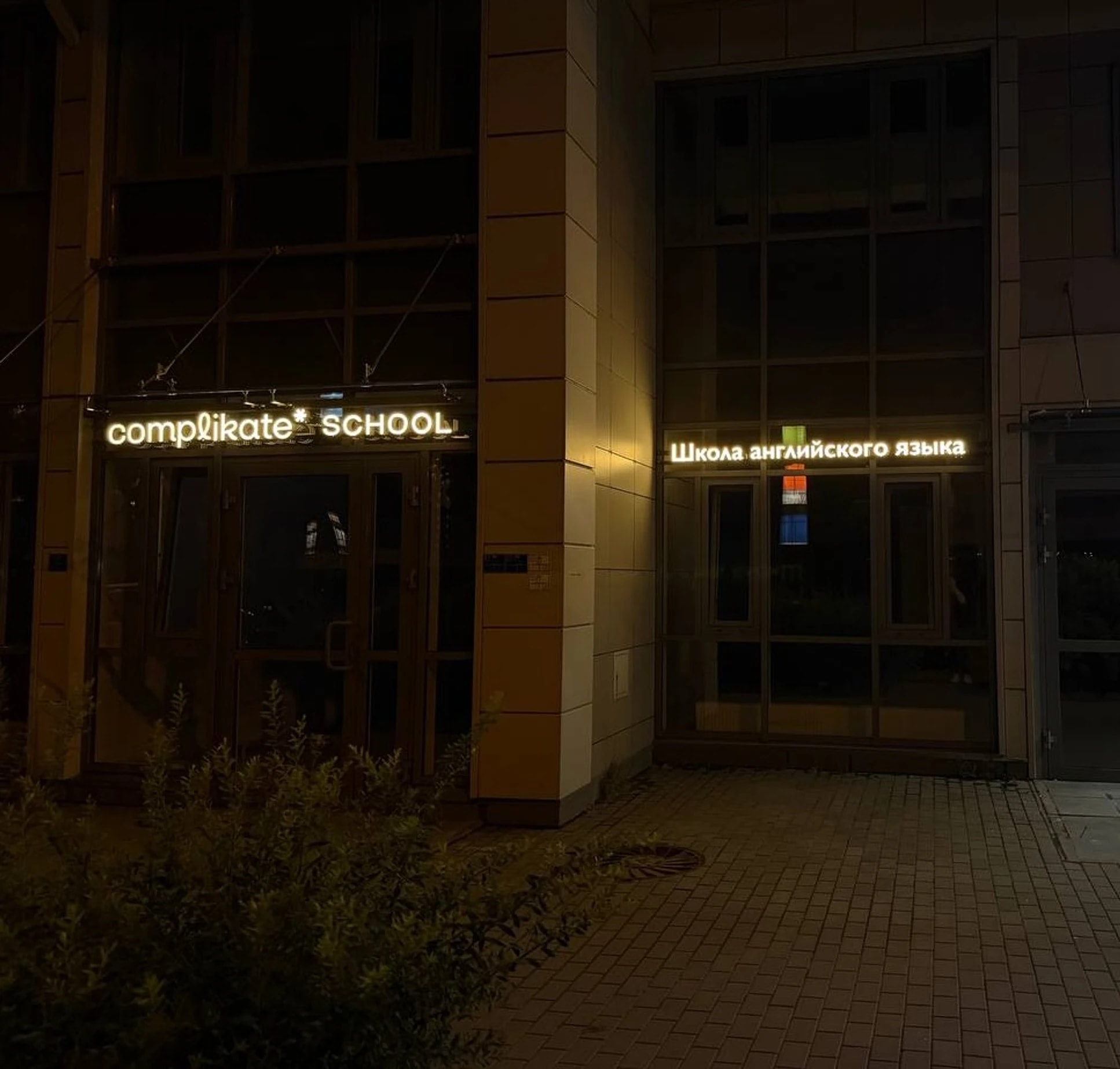 Объёмные буквы complikate SCHOOL и надпись «Школа английского языка» на фасаде Complikate School вечером, Среднерогатская ул., 11, Санкт-Петербург